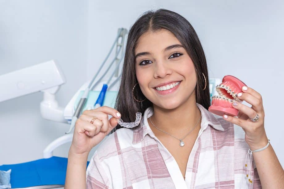 teen girl with straight teeth holding up Invisalign aligner and model with braces